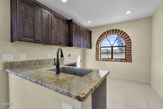 kitchen featuring sink, dark brown cabinetry, light tile patterned floors, light stone counters, and kitchen peninsula