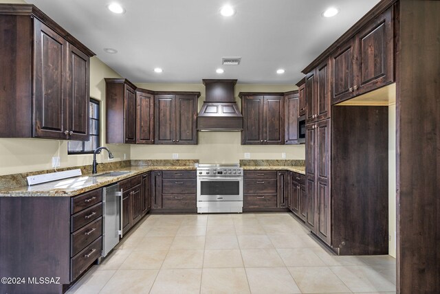 kitchen with premium range hood, light stone counters, dark brown cabinetry, stainless steel appliances, and sink