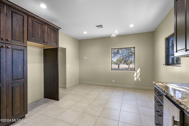 kitchen with light tile patterned floors, dark brown cabinetry, and stone countertops