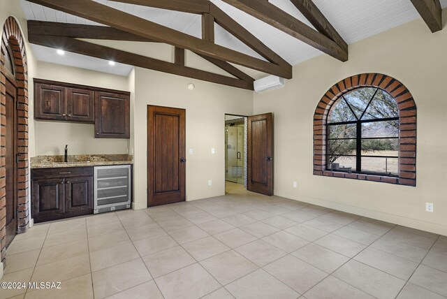 kitchen with sink, beverage cooler, vaulted ceiling with beams, light stone counters, and light tile patterned floors