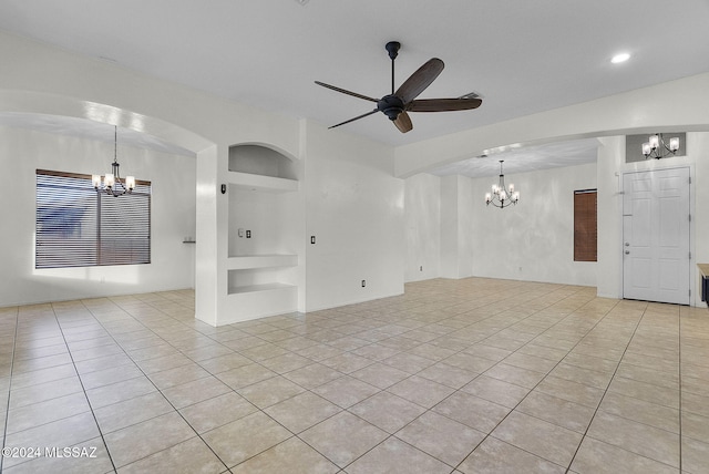 unfurnished living room with built in shelves, ceiling fan with notable chandelier, and light tile patterned floors