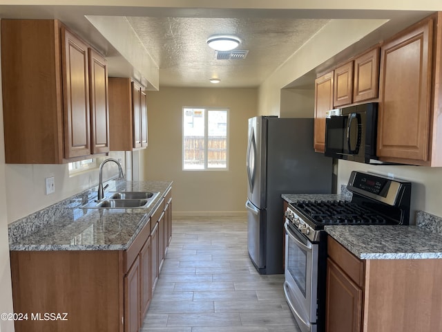 kitchen featuring light wood-type flooring, light stone counters, gas range, a textured ceiling, and sink