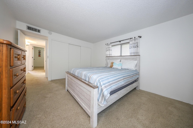 bedroom featuring light colored carpet, a textured ceiling, and a closet