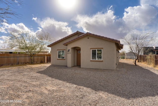 back of house with a tile roof, fence, and stucco siding