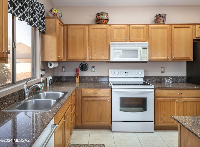 kitchen featuring white appliances, sink, light tile patterned floors, and dark stone counters