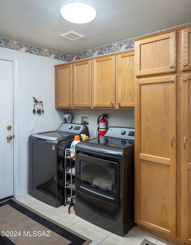 laundry room featuring washer and clothes dryer, light tile patterned floors, and cabinets