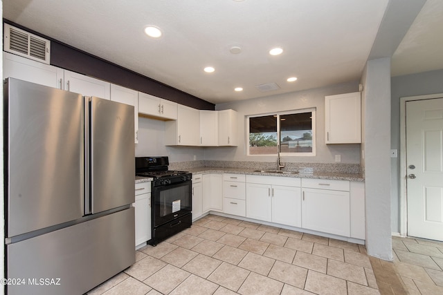 kitchen featuring gas stove, stainless steel refrigerator, white cabinetry, sink, and light stone counters