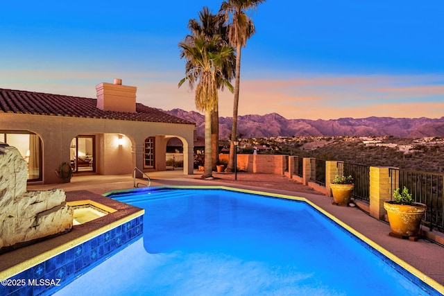 pool at dusk with a mountain view, a patio area, and an in ground hot tub