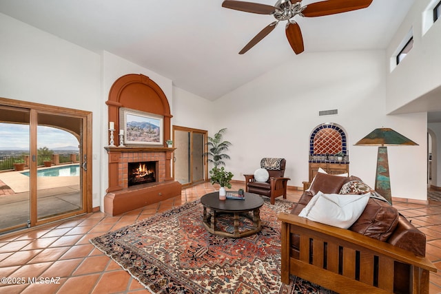 living room with a tile fireplace, ceiling fan, high vaulted ceiling, and light tile patterned floors