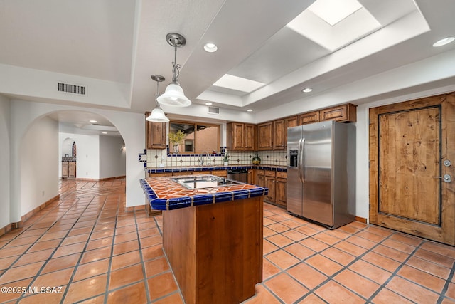 kitchen featuring kitchen peninsula, appliances with stainless steel finishes, decorative backsplash, a raised ceiling, and tile countertops