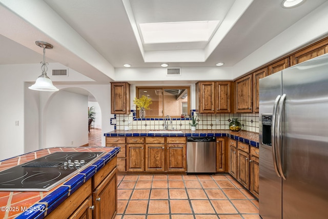 kitchen featuring a raised ceiling, sink, decorative backsplash, tile counters, and stainless steel appliances