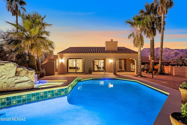 pool at dusk featuring an in ground hot tub, a mountain view, and a patio