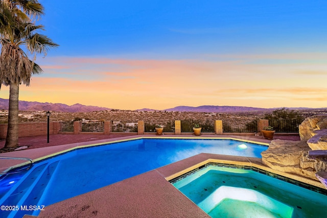 pool at dusk with an in ground hot tub and a mountain view