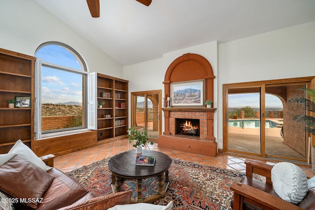 tiled living room with ceiling fan, high vaulted ceiling, and a tiled fireplace