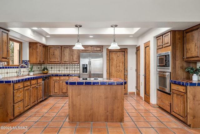 kitchen with hanging light fixtures, tile countertops, a center island, and stainless steel appliances