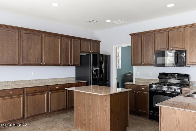 kitchen featuring black appliances, dark brown cabinetry, light stone counters, and a center island