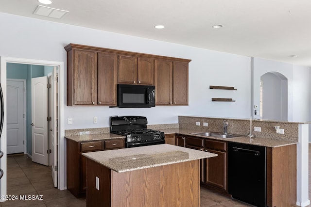 kitchen with light stone counters, sink, black appliances, and a kitchen island