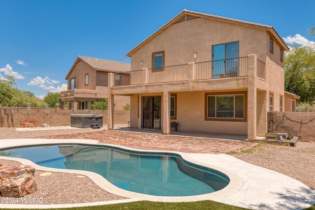 back of property with a balcony, a patio area, and a pool with hot tub