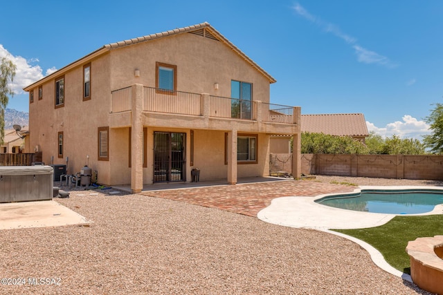 rear view of property with a patio area, a swimming pool with hot tub, and a balcony