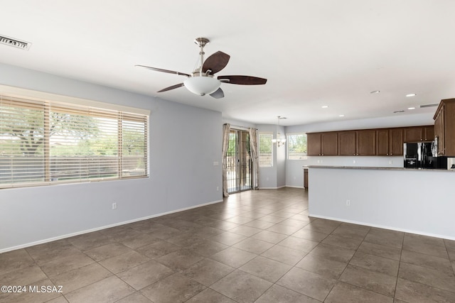 kitchen featuring ceiling fan with notable chandelier, hanging light fixtures, dark tile patterned floors, and black fridge with ice dispenser