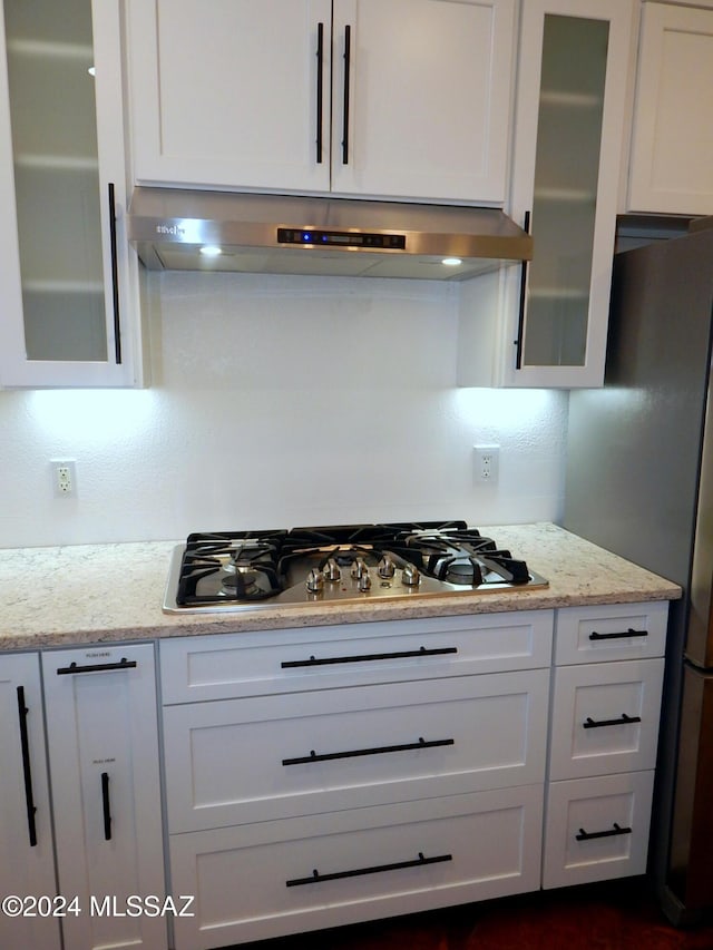 kitchen featuring light stone counters, white cabinets, stainless steel appliances, and ventilation hood