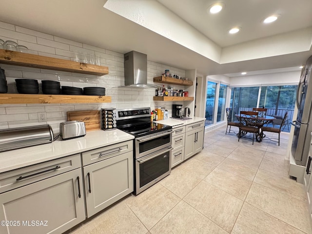 kitchen with gray cabinetry, backsplash, wall chimney range hood, light tile patterned floors, and appliances with stainless steel finishes