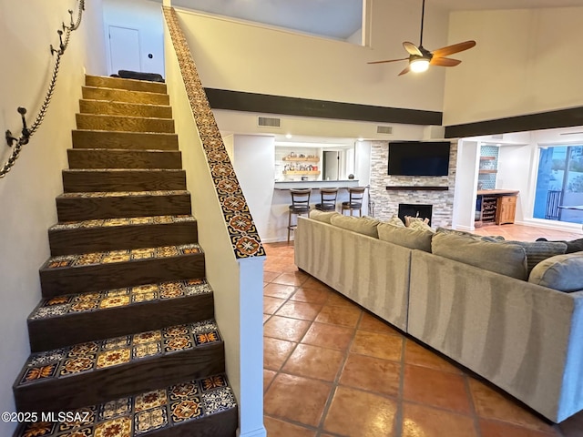 stairway with tile patterned flooring, high vaulted ceiling, ceiling fan, and a stone fireplace