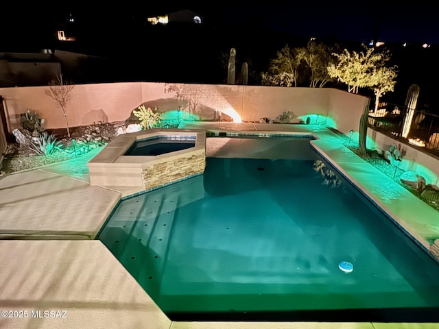 pool at night featuring an in ground hot tub