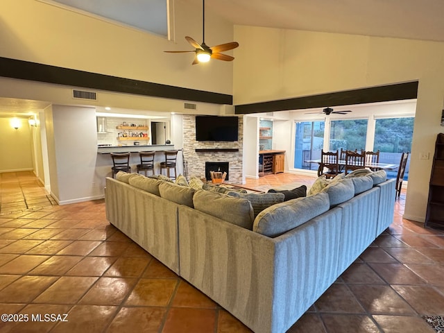 living room with tile patterned flooring, high vaulted ceiling, a stone fireplace, and ceiling fan