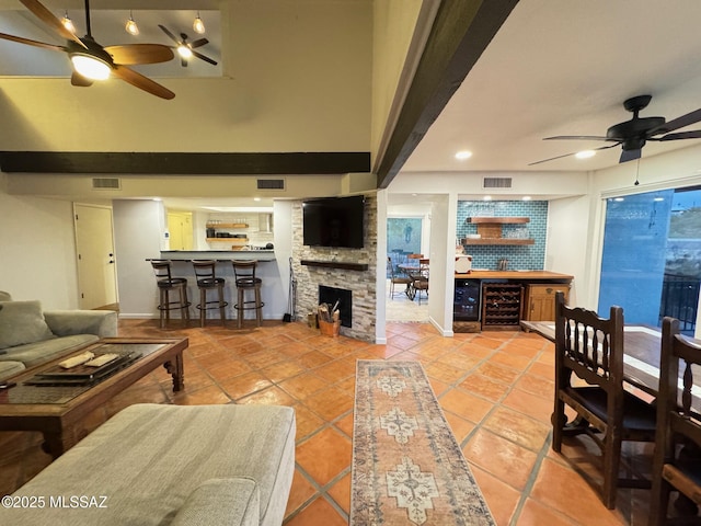 living room featuring ceiling fan, beverage cooler, a stone fireplace, bar area, and tile patterned floors