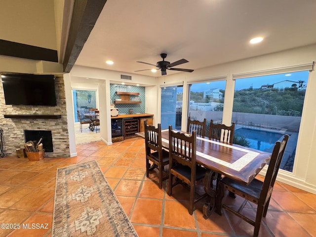 tiled dining room featuring bar, wine cooler, a stone fireplace, and ceiling fan