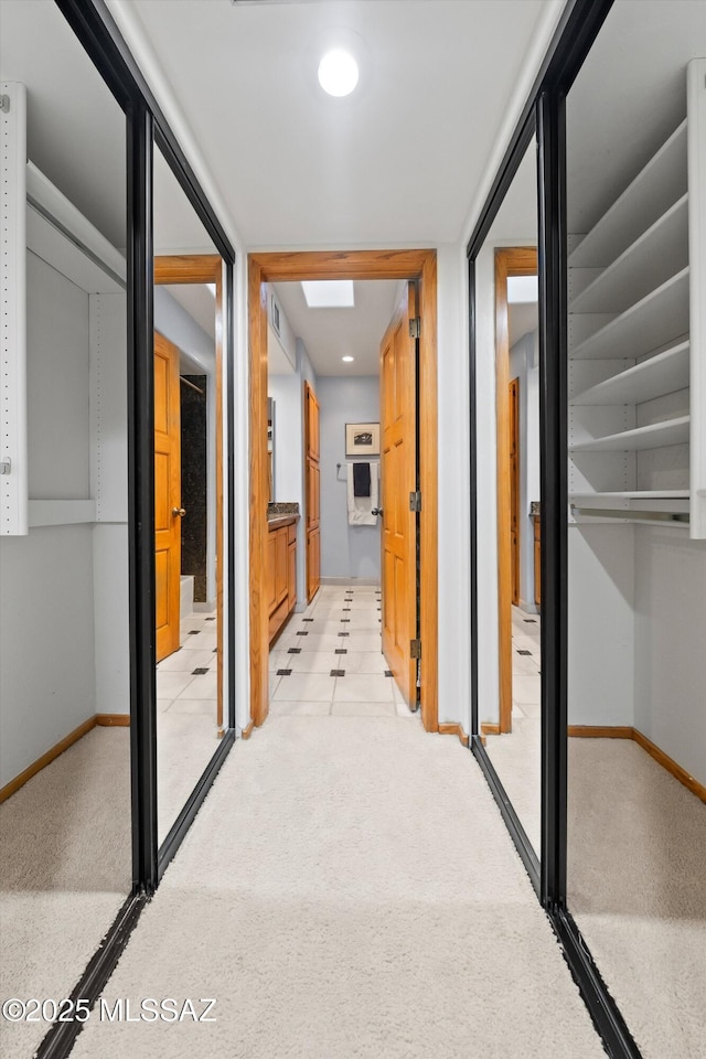 hall with a skylight, baseboards, and light colored carpet