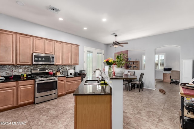 kitchen featuring decorative backsplash, dark stone counters, stainless steel appliances, ceiling fan, and sink