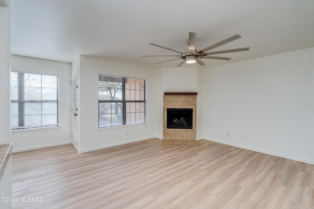 unfurnished living room featuring a tiled fireplace, ceiling fan, plenty of natural light, and light hardwood / wood-style flooring