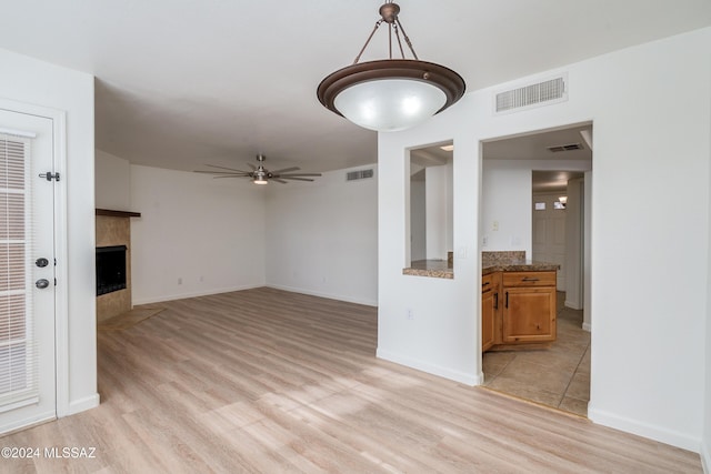 unfurnished living room featuring ceiling fan, light hardwood / wood-style floors, and a tile fireplace