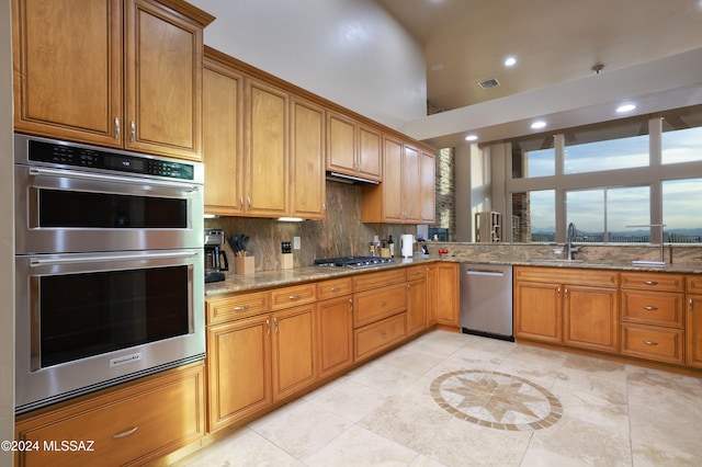 kitchen with sink, decorative backsplash, light tile patterned floors, light stone countertops, and appliances with stainless steel finishes