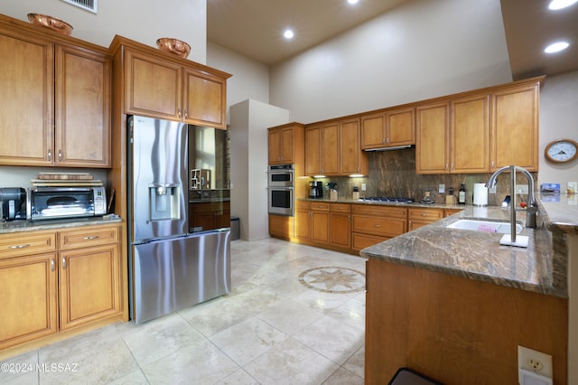 kitchen with kitchen peninsula, appliances with stainless steel finishes, sink, dark stone countertops, and a high ceiling