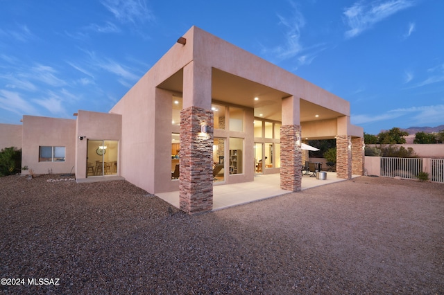 back house at dusk featuring a patio area and exterior fireplace