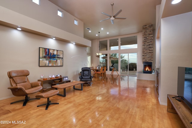 living area with light wood-type flooring, a towering ceiling, ceiling fan, and a fireplace