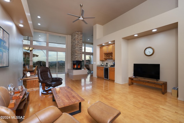 living room featuring ceiling fan, a high ceiling, a stone fireplace, bar area, and light wood-type flooring