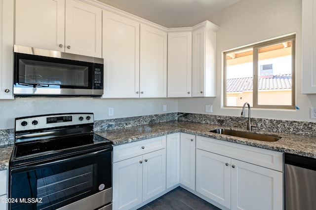 kitchen featuring white cabinets, sink, dark hardwood / wood-style floors, dark stone countertops, and appliances with stainless steel finishes