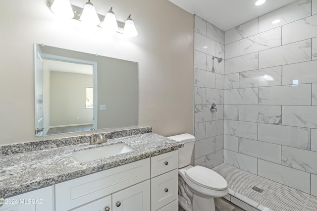 bathroom with a tile shower, vanity, and toilet