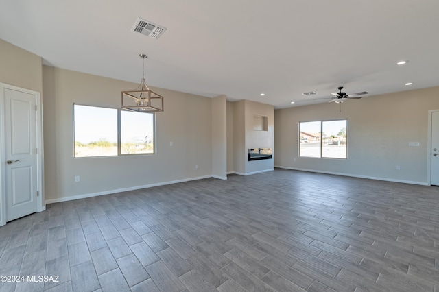 unfurnished living room featuring hardwood / wood-style floors and ceiling fan with notable chandelier