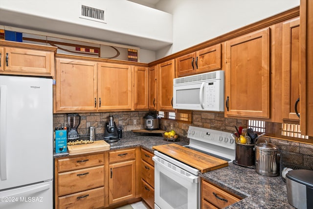 kitchen featuring white appliances, tasteful backsplash, and dark stone counters