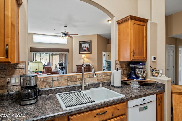 kitchen with ceiling fan, dishwasher, sink, dark stone countertops, and decorative backsplash