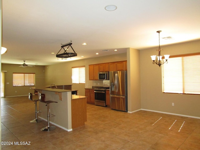 kitchen featuring ceiling fan with notable chandelier, hanging light fixtures, a breakfast bar area, light tile patterned floors, and stainless steel appliances