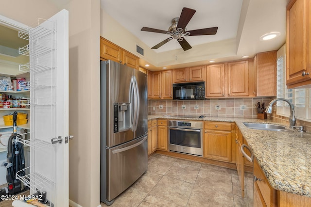 kitchen featuring light stone countertops, sink, ceiling fan, a tray ceiling, and black appliances