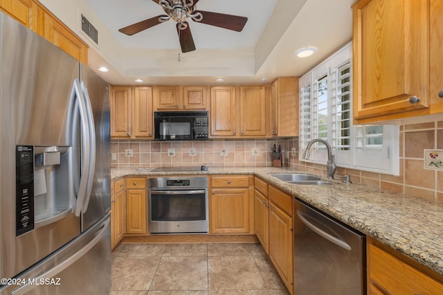 kitchen with ceiling fan, sink, light stone countertops, a tray ceiling, and black appliances