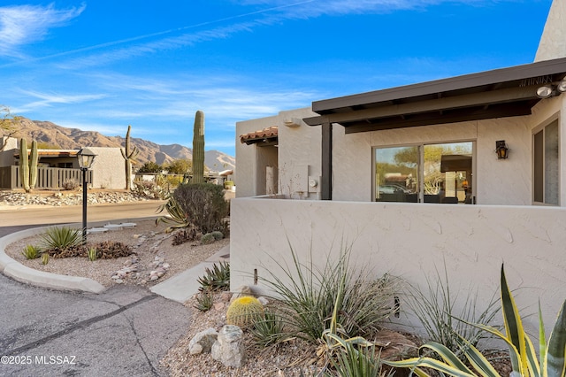 view of side of property with fence, a mountain view, and stucco siding