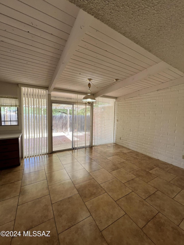 tiled spare room featuring beam ceiling and brick wall